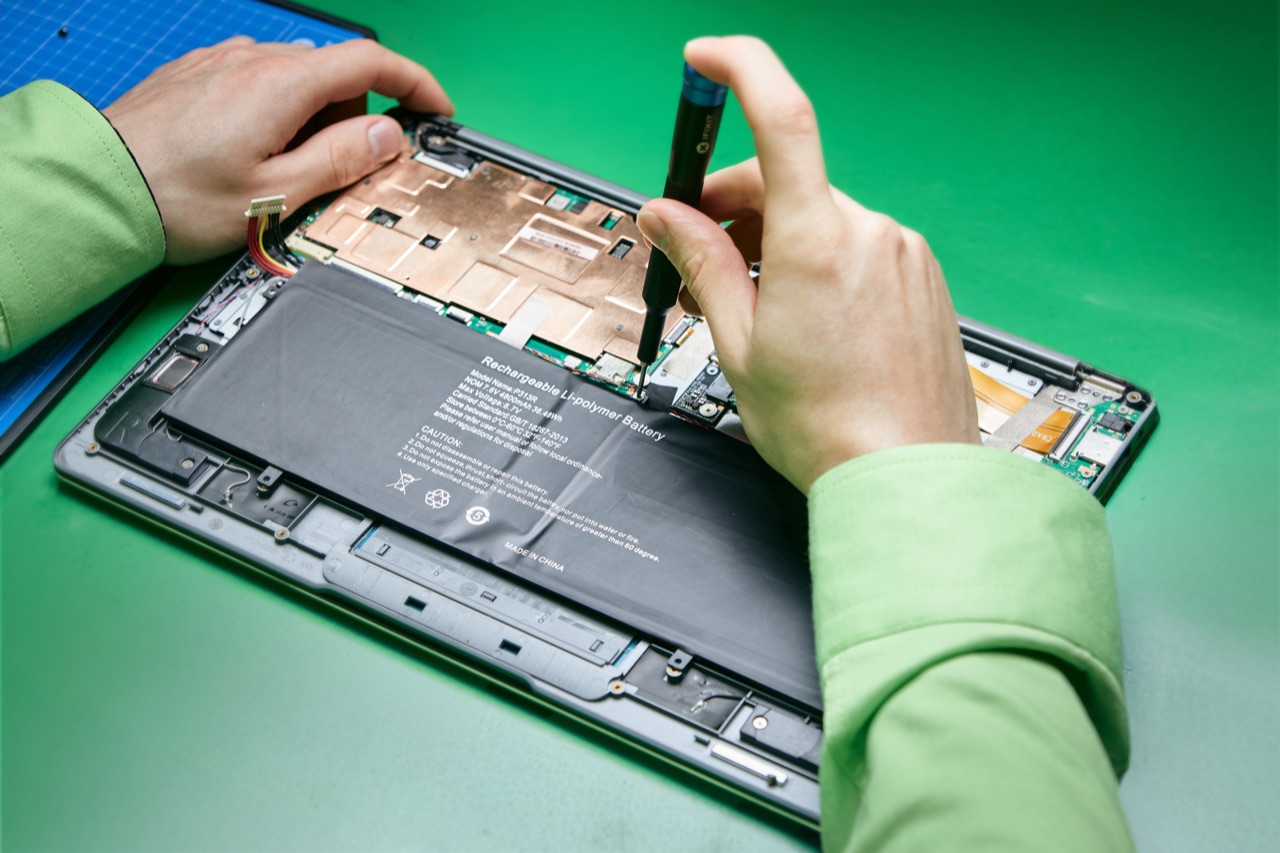 Hände im grünen Firmenhemd am geöffneten Notebook mit Schraubendreher